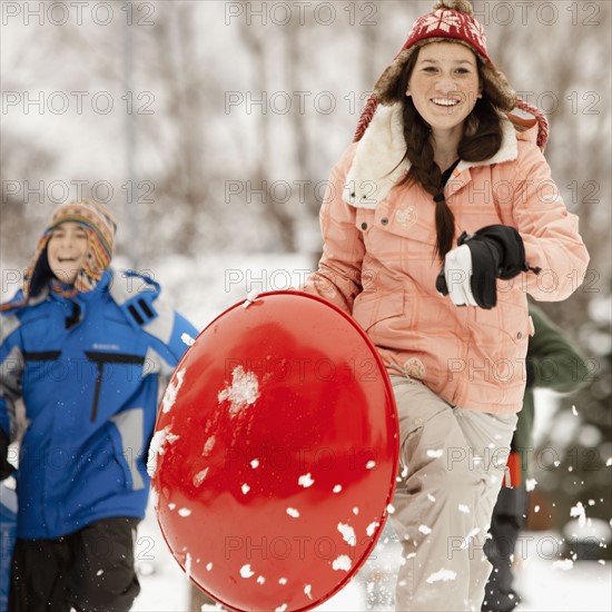 USA, Utah, Provo, Teenage (16-17) girl running with sledge, boys and girls (10-11, 12-13) in background. Photo : FBP