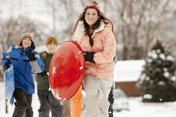 USA, Utah, Provo, Teenage (16-17) girl running with sledge, boys and girls (10-11, 12-13) in background. Photo : FBP