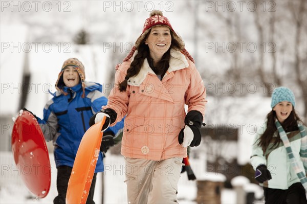 USA, Utah, Provo, Teenage (16-17) girl running with sledge, boys and girls (10-11, 12-13) in background. Photo : FBP