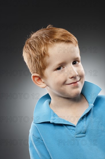 Portrait of smiling redhead boy (4-5) wearing blue polo shirt, studio shot. Photo : FBP