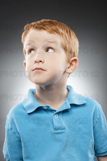 Portrait of smiling redhead boy (4-5) wearing blue polo shirt and looking up, studio shot. Photo : FBP