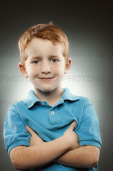 Portrait of smiling redhead boy (4-5) wearing blue polo shirt with arms crossed, studio shot. Photo : FBP