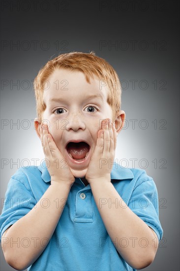 Portrait of smiling redhead boy (4-5) wearing blue polo shirt and looking surprised, studio shot. Photo : FBP