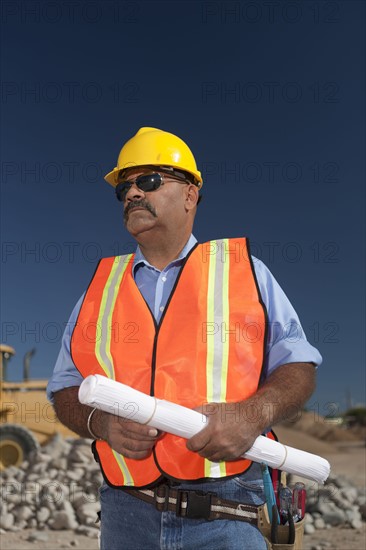Construction worker holding blueprint on building site. Photo : Dan Bannister