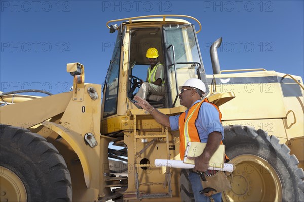 Two construction workers talking by mechanical digger. Photo : Dan Bannister