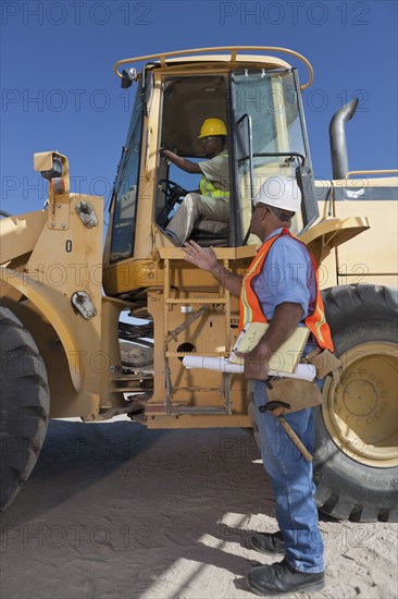 Two construction workers talking by mechanical digger. Photo : Dan Bannister