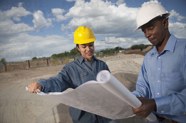 Two construction workers discussing blueprints on building site. Photo : Dan Bannister