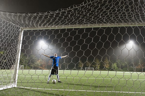 USA, California, Ladera Ranch, goalie on illuminated soccer field at night.