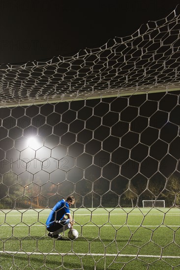 USA, California, Ladera Ranch, goalie on illuminated soccer field at night.