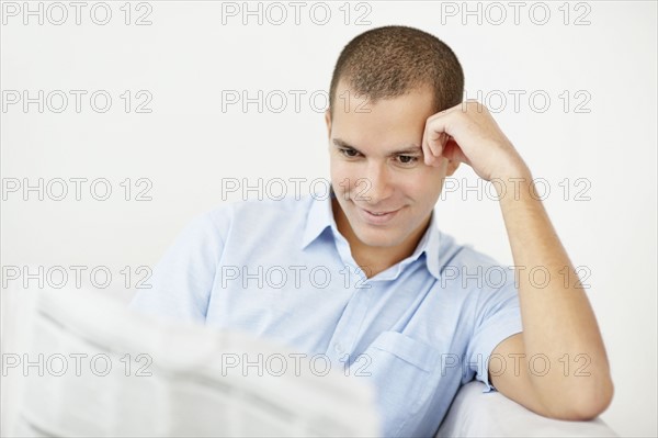 South Africa, Young smiling man reading newspaper. Photo : momentimages