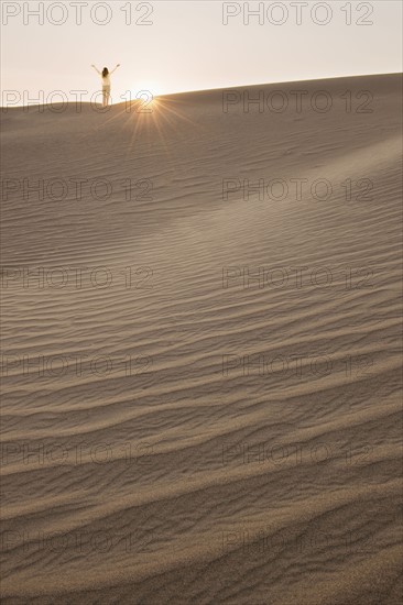 Woman with arms up, standing in desert.