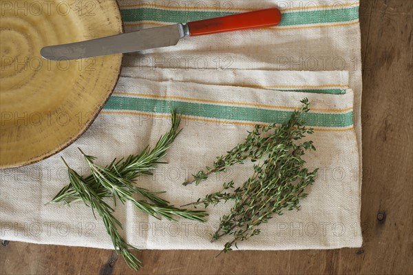 Rosemary and thyme with kitchen knife lying on kitchen cloth, directly above.