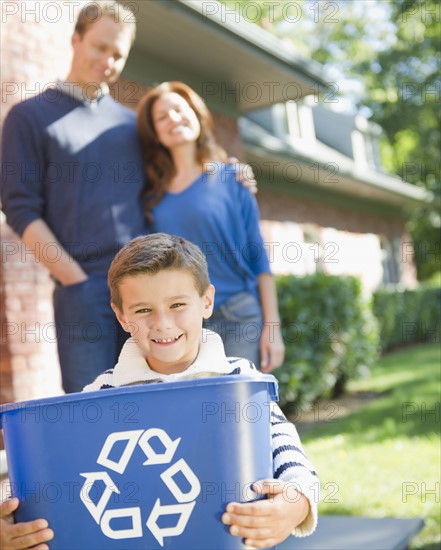 USA, New York, Flanders, Boy (8-9) holding bucket with recycling symbol, parents in background. Photo : Jamie Grill Photography