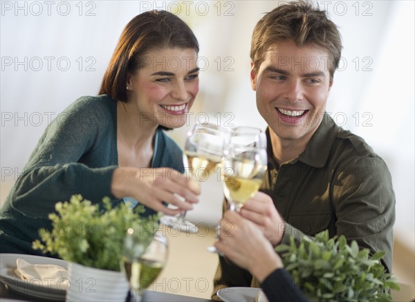 Couple toasting with white wine with third party in background.