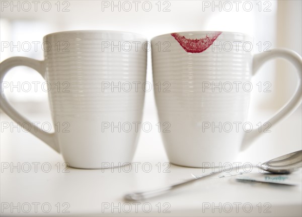 Close up of coffee mugs, one with red lipstick sign on edge. Photo : Jamie Grill Photography