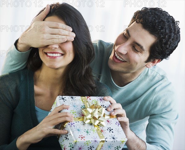 Young man giving his girlfriend present while covering her eyes. Photo : Daniel Grill