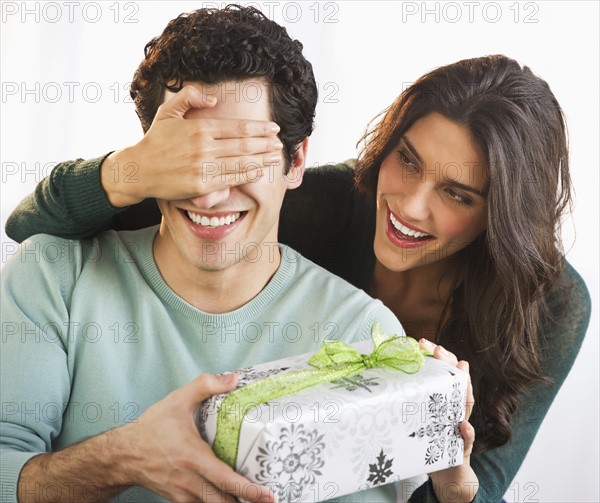 Young woman giving her boyfriend present while covering his eyes. Photo : Daniel Grill