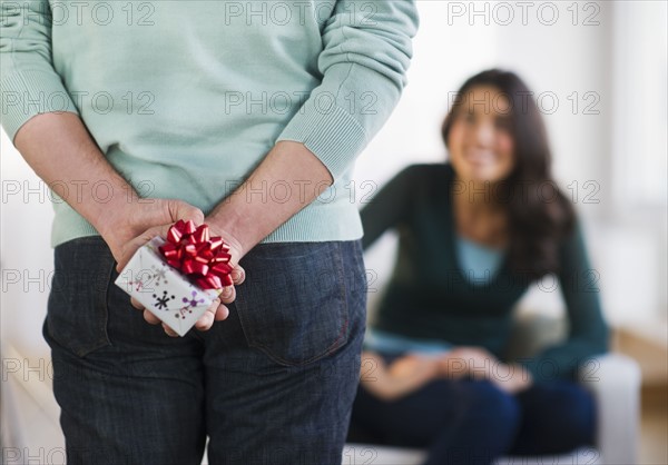 Young man with present behind his back, girlfriend in background. Photo : Daniel Grill