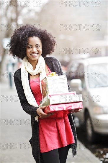 USA, Washington State, Seattle, Young cheerful woman carrying stack of boxed gifts. Photo : Take A Pix Media