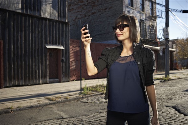 USA, New York City, Brooklyn, woman in street using phone. Photo : Shawn O'Connor