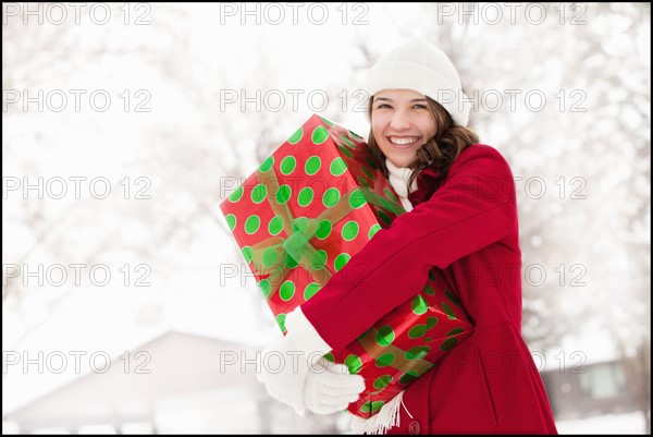 USA, Utah, Lehi, Portrait of young woman hugging Christmas gift outdoors. Photo : Mike Kemp