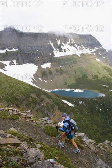 USA, Montana, Glacier National Park, Mid adult woman hiking with backpack during rain. Photo : Noah Clayton