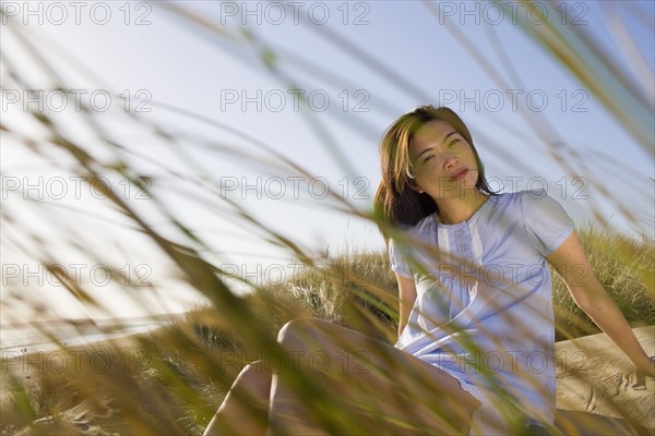 USA, California, Point Reyes, Young woman sitting in grass on sand dune. Photo : Noah Clayton