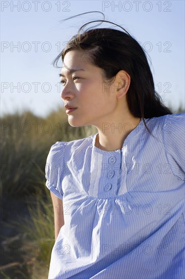 USA, California, Point Reyes, Young woman sitting in grass on sand dune. Photo : Noah Clayton