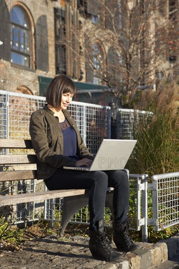 USA, New York City, Brooklyn, woman on bench using laptop. Photo : Shawn O'Connor
