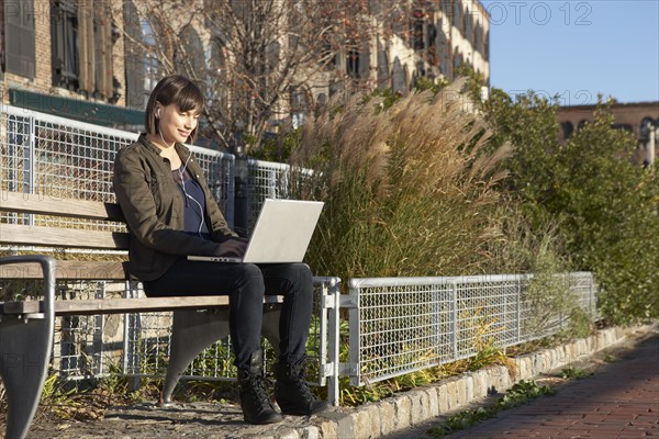 USA, New York City, Brooklyn, woman on bench using laptop. Photo : Shawn O'Connor