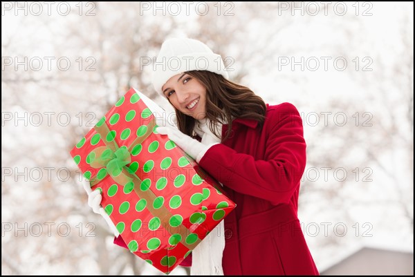 USA, Utah, Lehi, Portrait of young woman holding Christmas gift outdoors. Photo : Mike Kemp