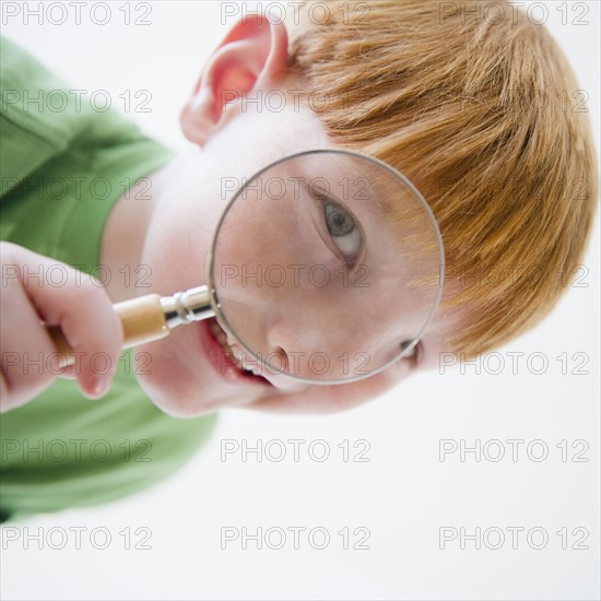 Portrait of boy (8-9) looking through magnifying glass. Photo : Jamie Grill Photography