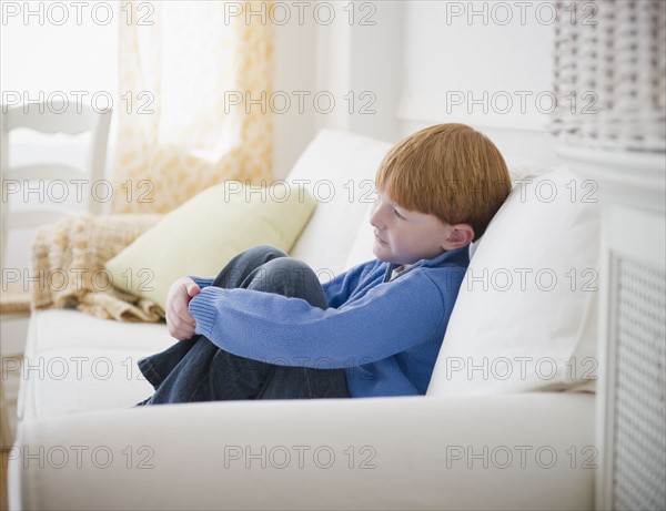 Boy (8-9) sitting on sofa. Photo : Jamie Grill Photography