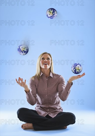 Young woman juggling globes in clouds. Photo : Daniel Grill