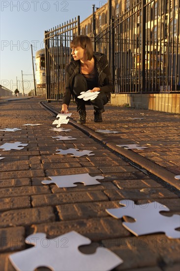 USA, New York City, Brooklyn, woman picking up jigsaw pieces from sidewalk. Photo : Shawn O'Connor