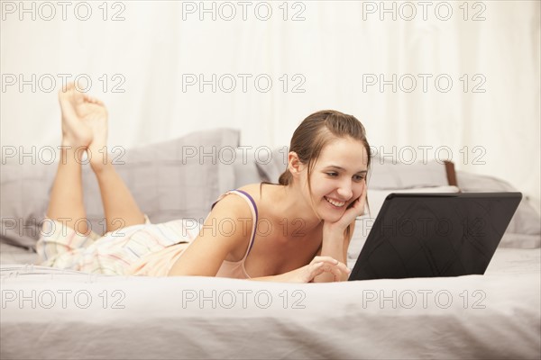 Young woman using laptop on bed. Photo : Mike Kemp