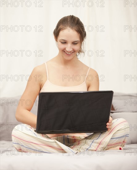 Young woman using laptop on bed. Photo : Mike Kemp