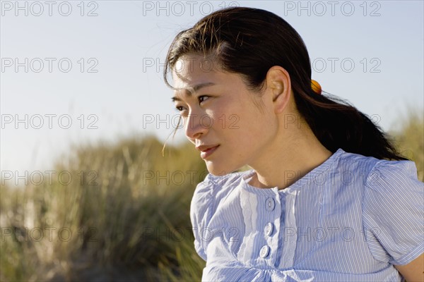 USA, California, Point Reyes, Young woman sitting in grass on sand dune. Photo : Noah Clayton