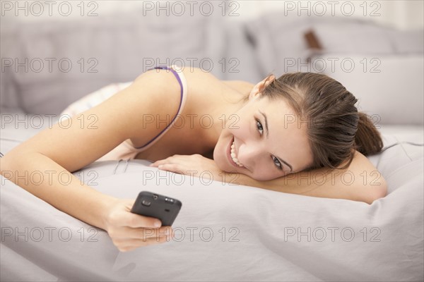 Portrait of young woman using mobile phone on bed. Photo : Mike Kemp