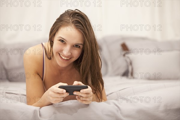 Portrait of young woman using mobile phone on bed. Photo : Mike Kemp