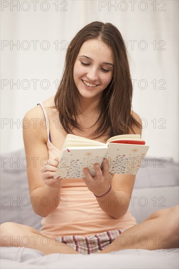 Young woman reading diary on bed. Photo : Mike Kemp