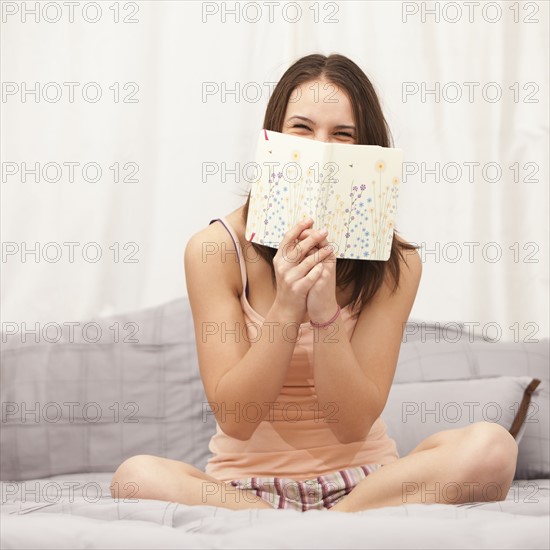 Young woman reading diary on bed, laughing. Photo : Mike Kemp