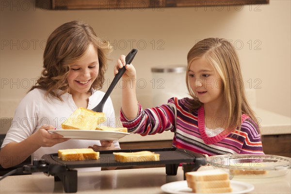 Two girls (10-11) preparing toast in kitchen. Photo : Mike Kemp