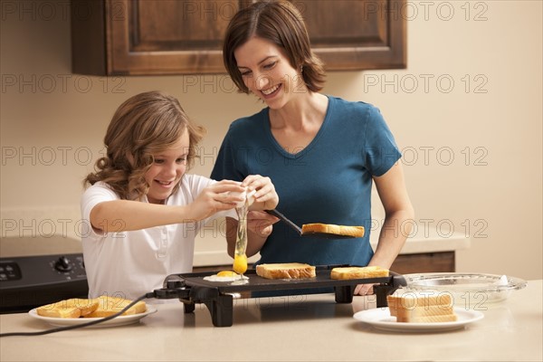 Mother preparing breakfast with daughter (10-11) in kitchen. Photo : Mike Kemp