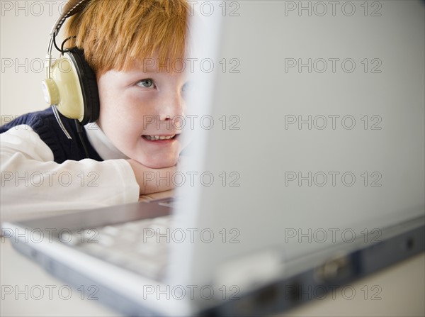 Boy (8-9) wearing headphones, using laptop. Photo : Jamie Grill Photography