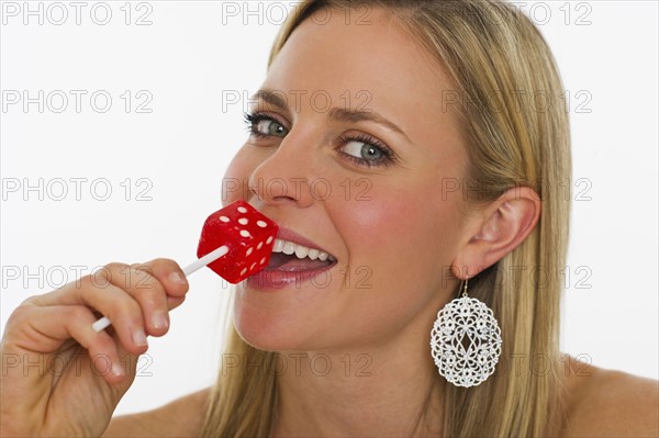 Studio portrait of young woman eating dice lollipop. Photo : Daniel Grill