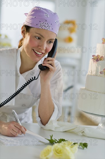 Happy young woman taking order near wedding cake.