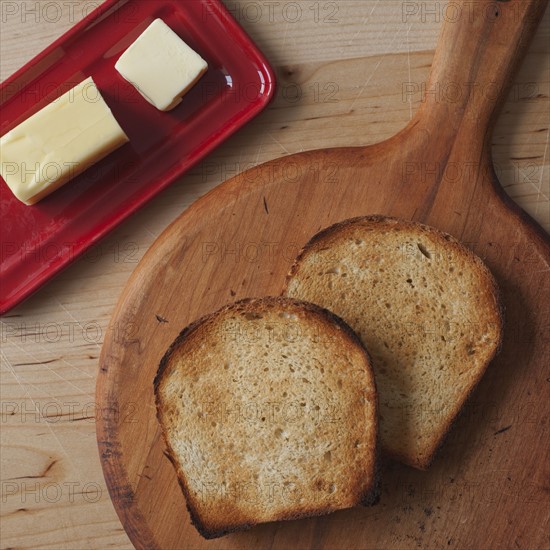 Close up of butter and toasted bread slices on cutting board .