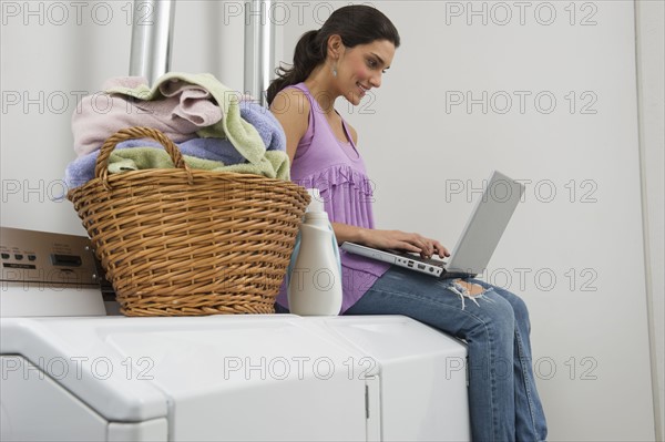 Woman doing laundry and using laptop.