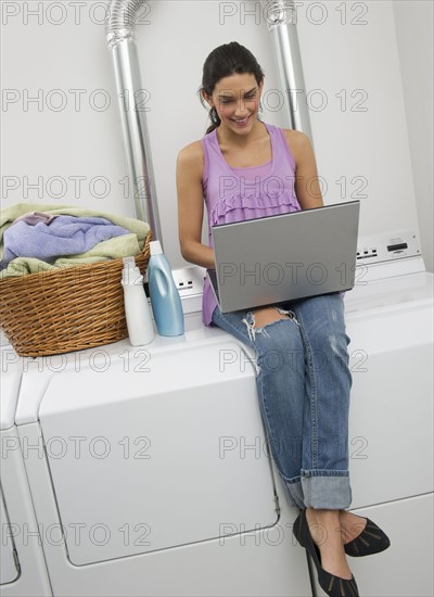 Woman doing laundry and using laptop.